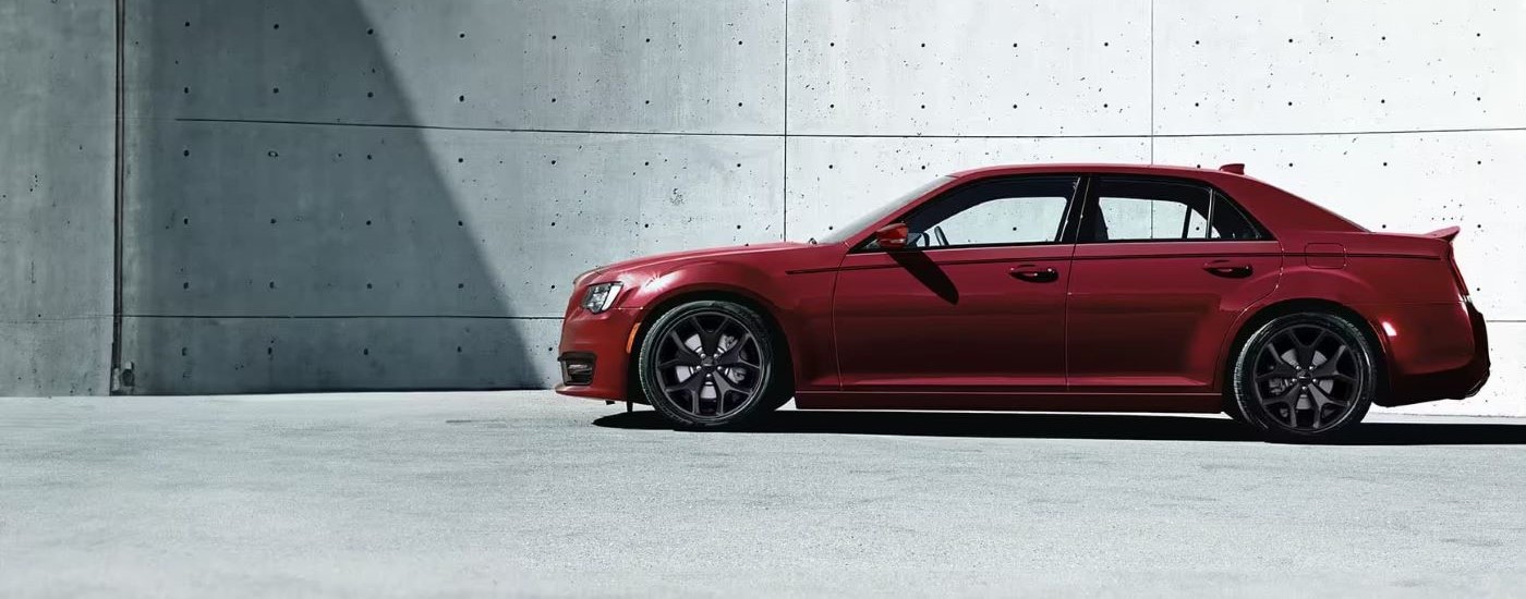 A red 2023 Chrysler 300 is shown from the side in front of a concrete wall.