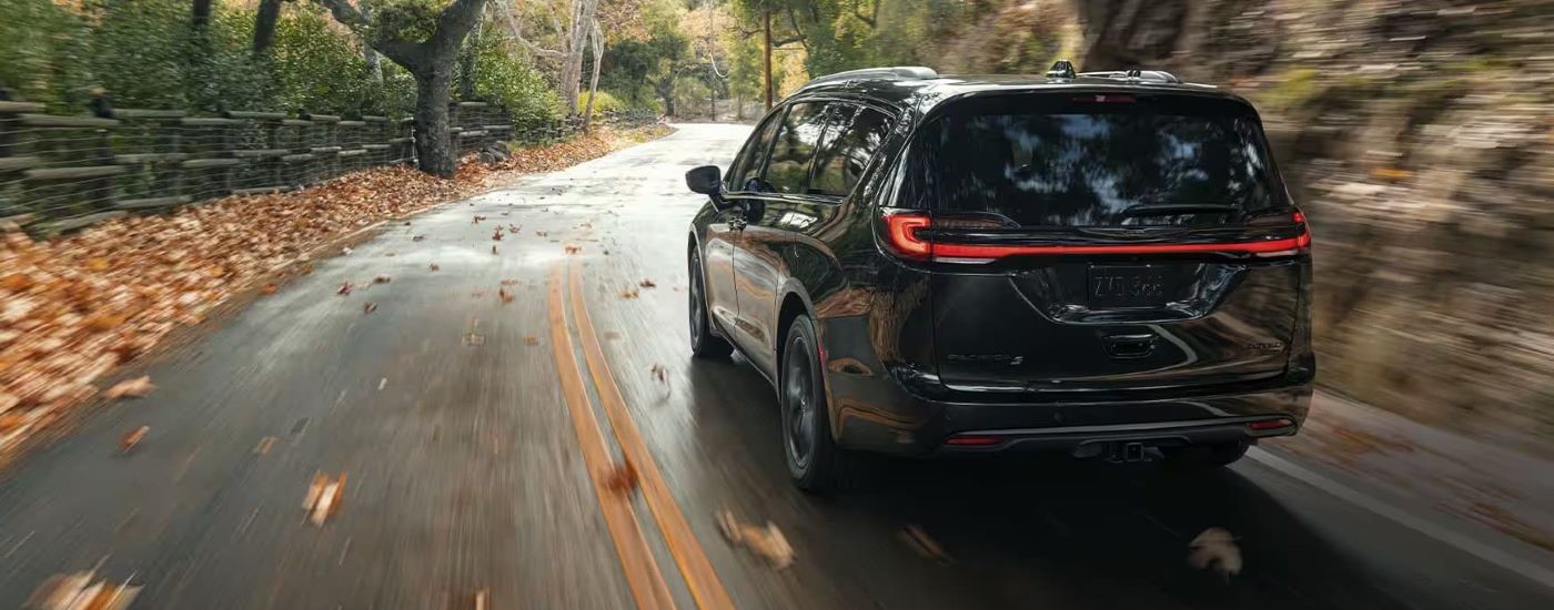 A black 2023 Chrysler Pacifica is shown rounding a corner after leaving a Chrysler dealer.