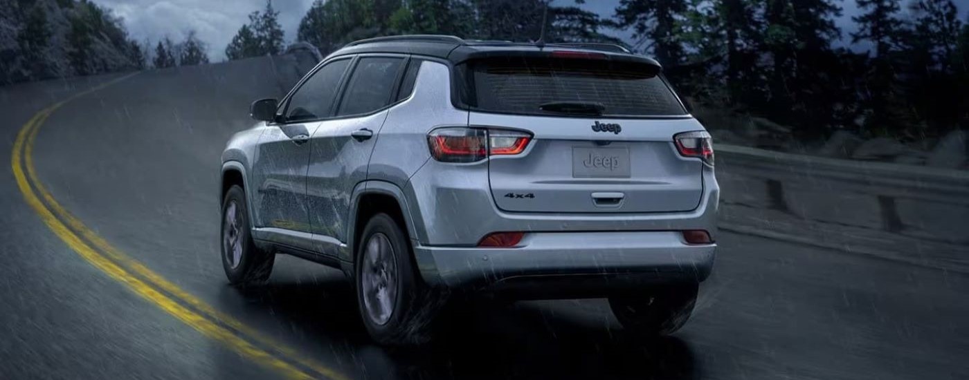 A silver 2023 Jeep Compass is shown driving around a corner at night.