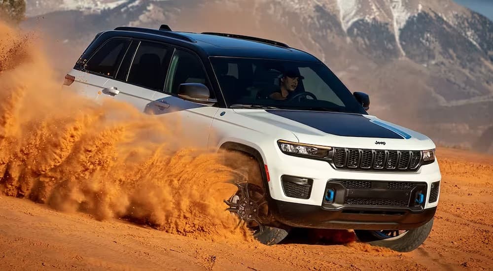A white 2024 Jeep Grand Cherokee 4xe is shown from the front at an angle while driving through sand.