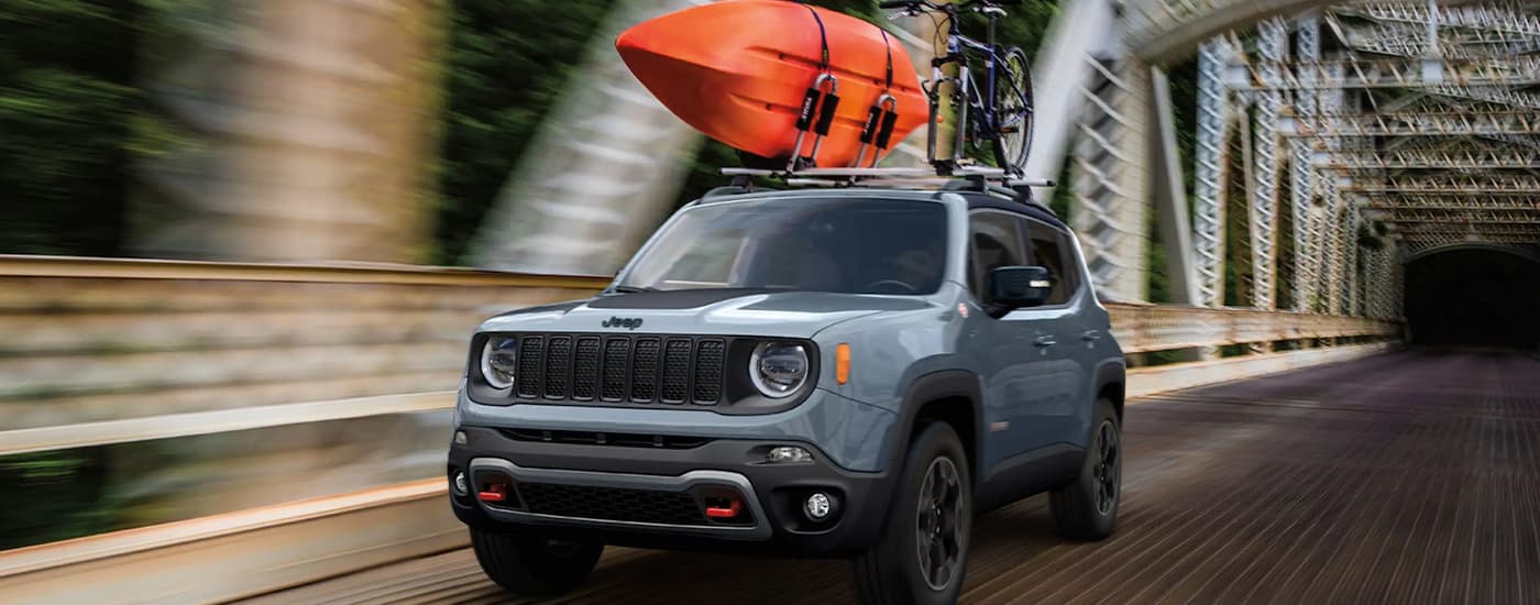 A grey 2023 Jeep Renegade is shown driving over a bridge with a kayak.