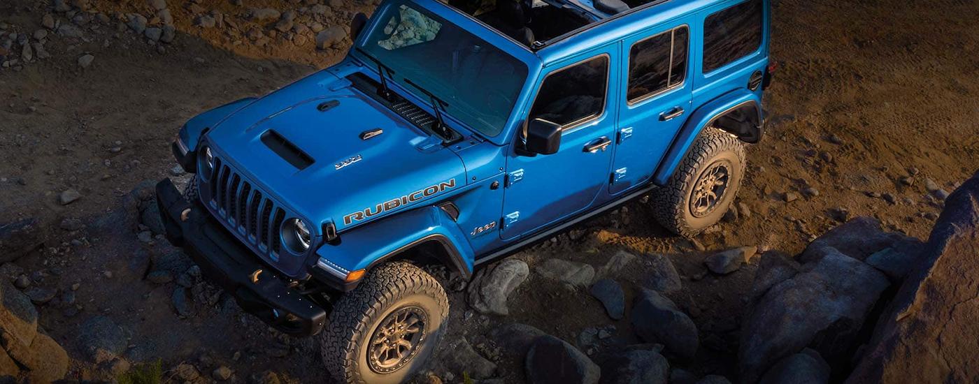 A blue 2023 Jeep Wrangler Rubicon is shown from a high angle driving on a rocky dirt trail.