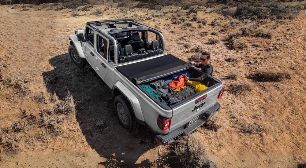 A person is shown stowing gear in the bed of a grey 2024 Jeep Gladiator.