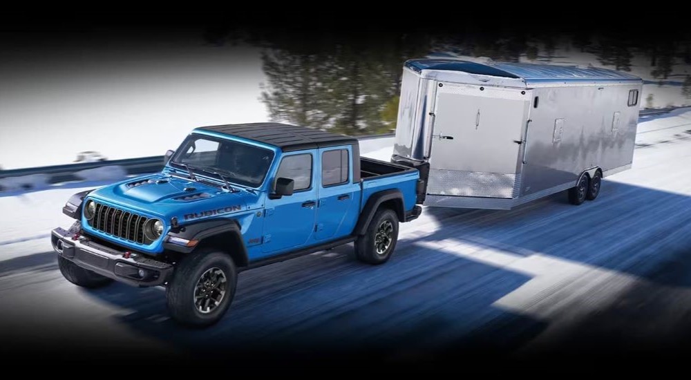 A blue 2023 Jeep Gladiator is shown towing a trailer on a snowy road.
